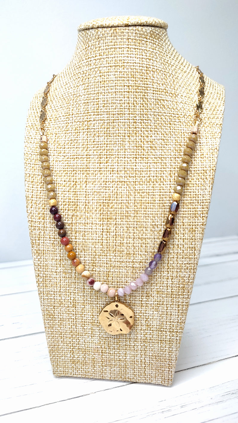 Collar en tonos tierras y morado con medalla de acero bañada en oro con flor labrada