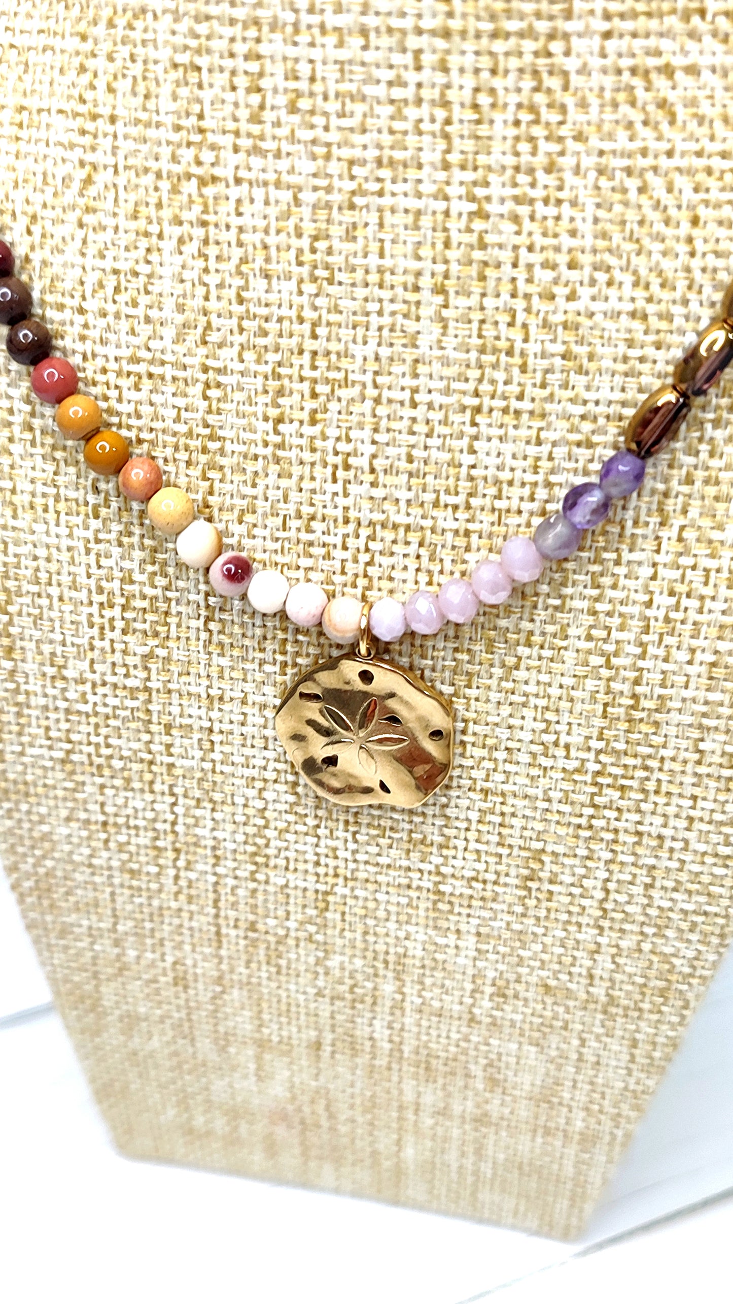 Collar en tonos tierras y morado con medalla de acero bañada en oro con flor labrada