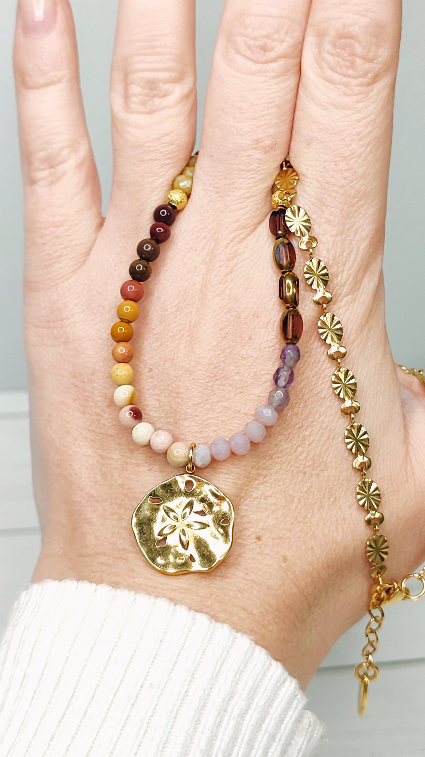 Collar en tonos tierras y morado con medalla de acero bañada en oro con flor labrada