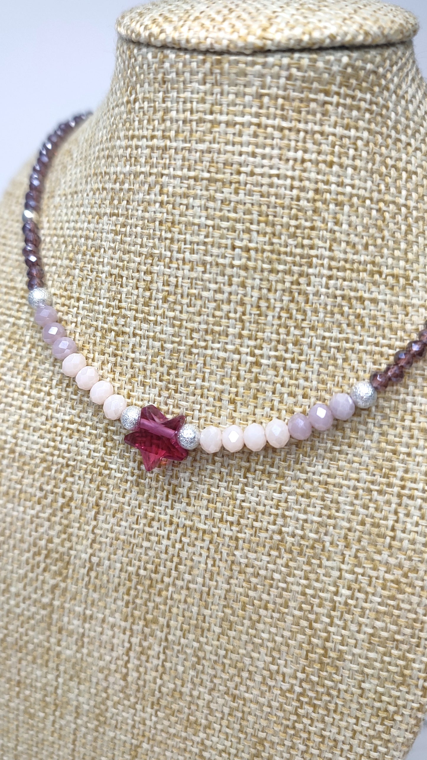 Detalle en el busto delCollar realizado en distintos tipos de cristales en tonos malva y rosa, cuenta con una estrella de cristal en el centro.