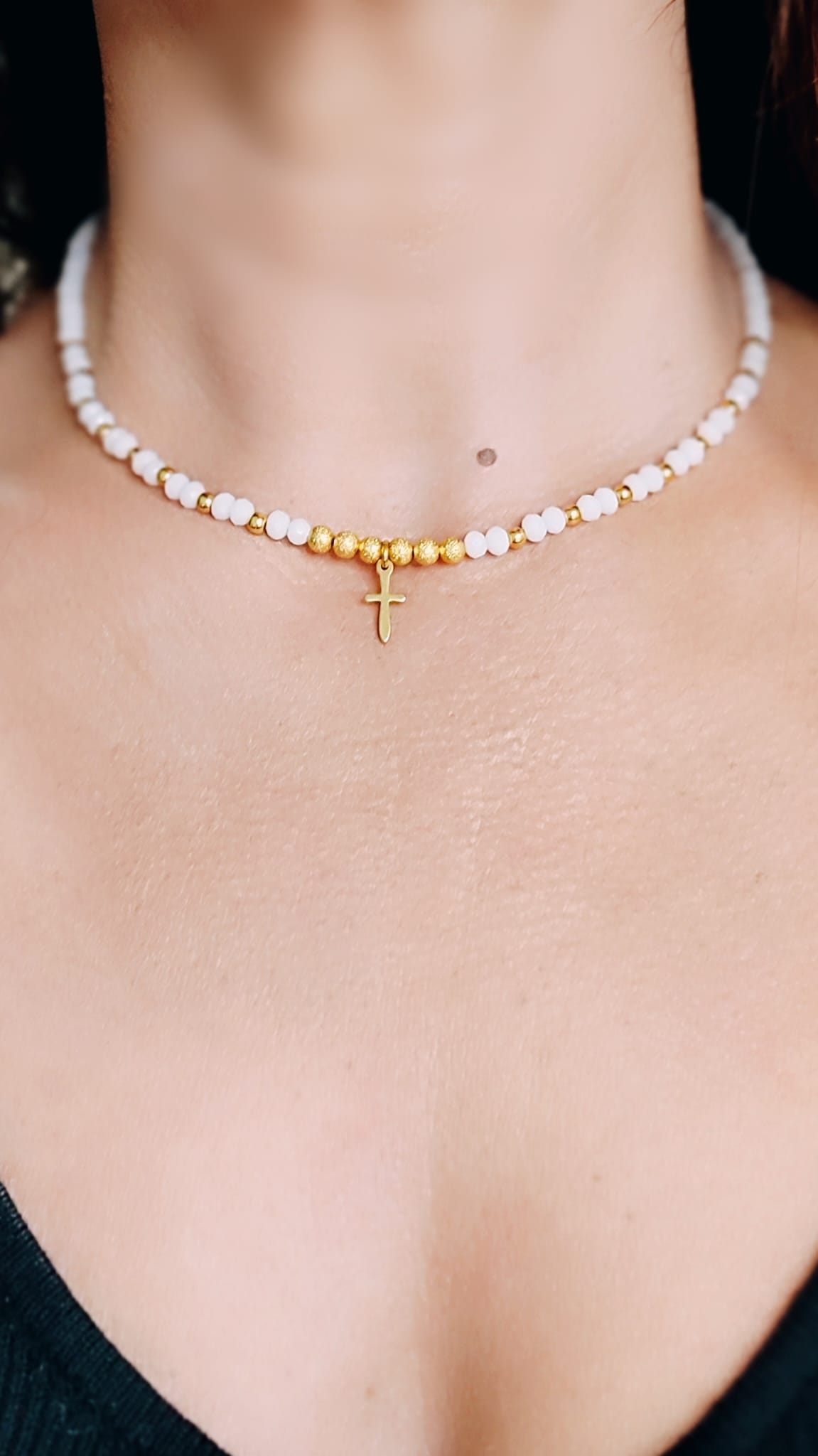 Vista en el escote del Collar de cristal blanco y bolitas doradas mate, en el centro tiene una pequeña cruz de acero bañada en oro