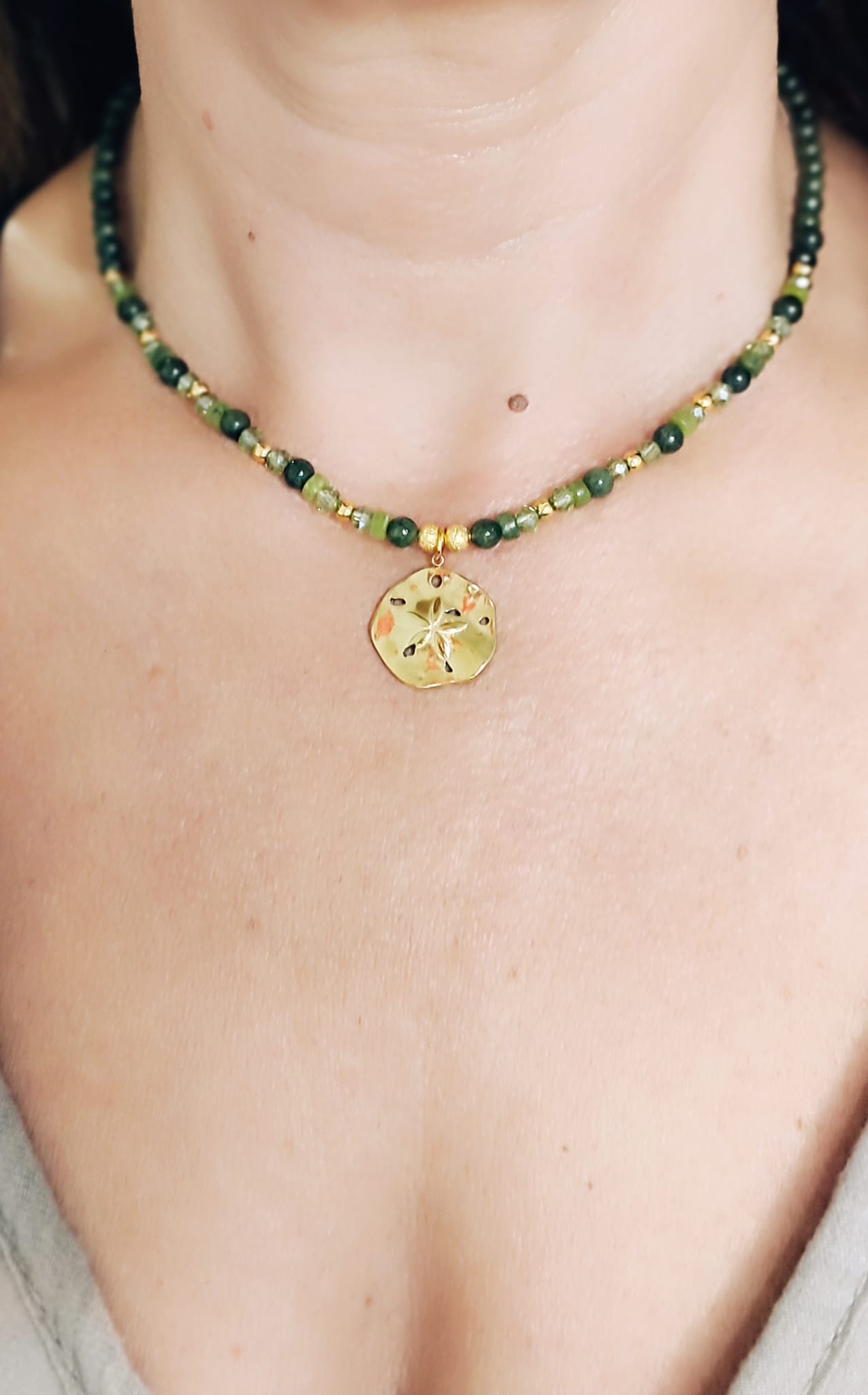 Aqui se aprecia con queda puesto en el escote el Collar de Minerales en tonos verde con medalla rustica dorada con flor en el centro