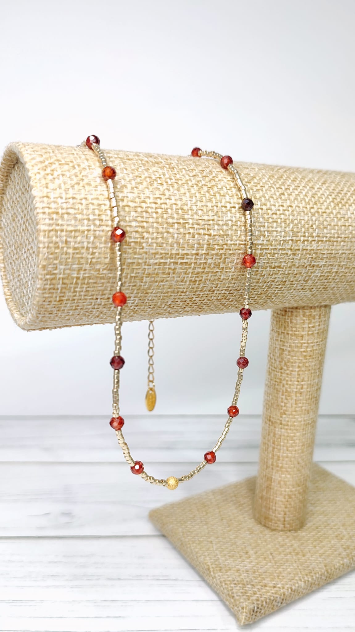 Elegante collar compuesto por circonios rojos y pequeñas delicas doradas, en el centro, una bolita dorada