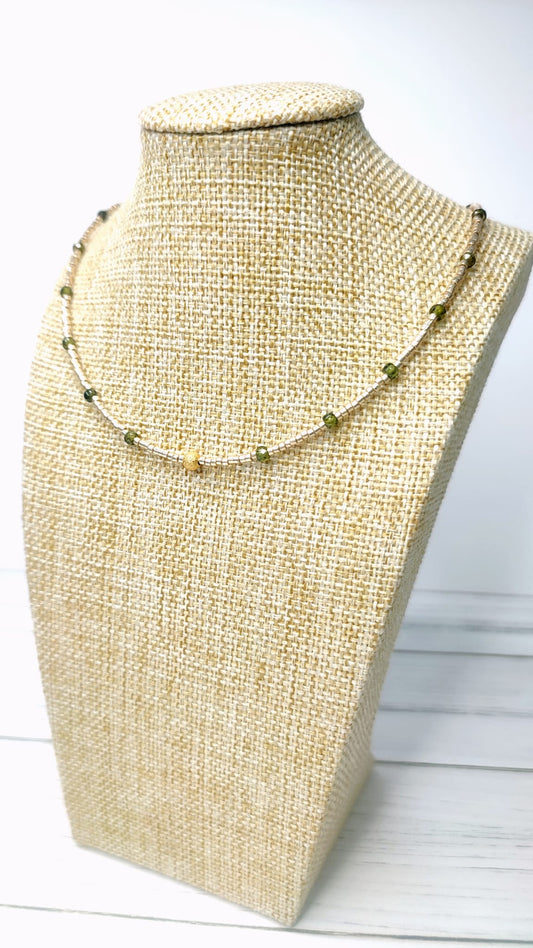 Elegante collar compuesto por circonios verde oliva y pequeñas delicas doradas, en el centro, una bolita dorada